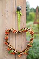 A woven heart wreath with Pyracantha berries hanging on a door with a view to garden