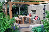 Outdoor seating and dining area with open pergola, wooden table and wall mounted water feature