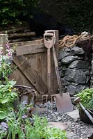 Old tools in the Motor Neurone Disease - A Hebridean Weavers Garden - wooden gate, garden fork, spade, bucket of sea weed and stone wall