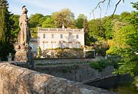 Iford Manor, a Georgian house, sitting in a steep sided valley beside the River Frome, seen from the bridge, dating from 1400, topped by an 18th century statue of Britannia installed by Peto