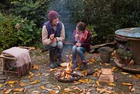 Mother and daughter roasting marshmallows over a firepit in an autumnal back garden.