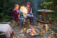 Mother and daughter lighting sparklers by a firepit in an autumnal back garden.