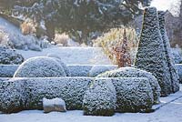 Parterre covered in snow, winter. Clipped topiary shapes in Box and Yew.  Sculpture in stone by Briony Lawson. 