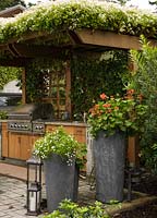 Clematis terniflora growing over wooden pergola sheltering outdoor kitchen. Lobelia 'Laguna White' and Pelargonium in pots