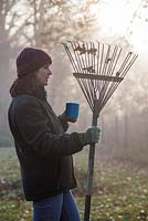 Woman holding rake and tea with view of morning sun