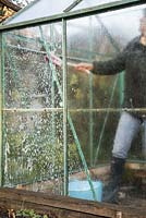 Woman using soapy water and a brush to clean greenhouse windows