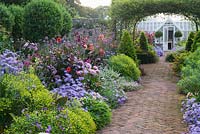Central brick path in the walled garden is framed by asters, dahlias, euphorbia, Verbena bonariensis and clipped bay pyramids. Alitex greenhouse is seen framed by a central rose arch clothed with Rosa banksiae. 