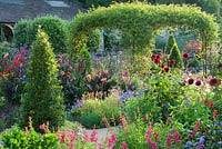Standard olives, clipped bay pyramids and rose arch clad with Rosa banksiae surrounded by exuberant planting including dahlias, salvias, gladioli, penstemons, ageratum, osteospermum and Verbena bonariensis. 