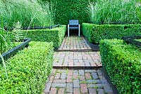 The Cornfield Garden with Calamagrostis x acutifora 'Overdam' surrounded by Box hedges  and contained by Yew hedges. Hand made brick paths. Veddw House Garden, Devauden, Monmouthshire, Wales. July