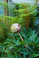 Mosaic ball on stick, designed by Anne Cardwell, in the border with ferns and Acanthus leaves in town garden