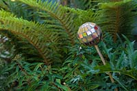 Mosaic ball on stick, designed by Anne Cardwell, in the border with ferns and Acanthus leaves in town garden