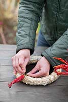 Woman securing dried red chillis to a wreath with pins
