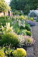 Formal herbaceous bed in Potager garden with Euphorbia, Sedum, Iris, Delphinium, Allium, Nepeta, Lupinus, Rosa, Papaver and Veronicastrum. Farleigh House, Hampshire