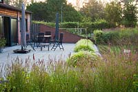 Furniture on terrace. Borders of prairie planting. Persicaria amplexicaulis 'Taurus', Hakonechloa macra, Molinia caerulea 'Edith Dudszus'. 