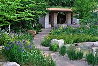 The Homebase Garden. RHS Chelsea Flower Show 2014. Stone path leading to Contemporary Pavillion with living roof. Iris sibirica, trollius and Aqulegia. 