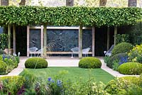 The Telegraph Garden, RHS Chelsea Flower Show 2014, gold medal winner. View of the patio with white modern metal chairs among trees Tilia x europaea 'Pallida', hedges Laurus nobilis,  Iris germanica and topiary Buxus sempervirens, Gladiolus italicus byzantinus, Stipa gigantea.