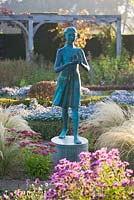 The hedged in formal garden at dawn with box and berberis hedging and topiary - girl statue called the 'lamp of wisdom'. Waterperry Gardens, Oxfordshire
