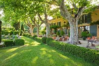 The house with plane trees, table and chairs on gravel terrace and hedging. Les Confines, Provence, France