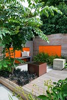 Modern contemporary garden in Brighton with decking, orange panels on walls, metal water feature, Ophiopogon and Aralia. 