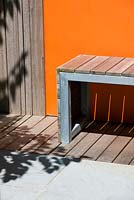 Modern contemporary garden in Brighton with decking, orange panels on walls, wooden bench and shadows