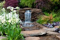 Cascading stream and stone bridge with planting of Acer, Agapanthus, Heuchera fern and Leucanthemum in The Water Garden - RHS Tatton Park Flower Show 2013.