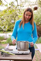 Woman making organic pesiticide made of rhubarb. Mixture of 500 g rhubarb leaves and 2,5 l of water boil for 20 minutes then remove from heat and cool.