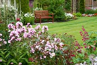 Herbaceous border with Phlox paniculata 'Bright Eyes', Penstemon 'Garnet',  Monarda 'Cambridge Scarlet',  Campanula lactiflora 'Loddon Anna', Veronicastrum virginicum 'Album' and Rosa 'A Whiter Shade of Pale' with seating area and bench and lawn beyond