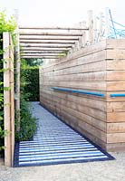 Corridor of wooden fences. Entrance of the garden Synthese is a path of bricks painted in stripes in dark blue, purple and white.