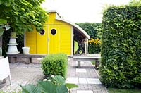 Bright yellow shed with roundshaped windows. Rudbeckia fulgida Goldsturm in the border.
