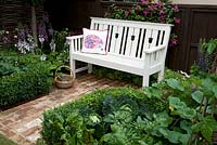 Hedgehog Street white wooden bench set on brick path flooring between box-edged vegetable beds with cabbage and potatoes.  Designer: Tracy Foster Sponsor: People's Trust for Endangered Species. Gold award  