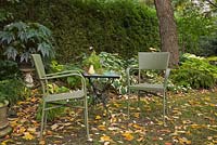 Fallen tree leaves and green wicker chairs and table in a backyard garden in autumn. Hosta - Plaintain lily plants in the background. Il Etait Une Fois garden, Monteregie, Quebec, Canada. 