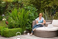 Garden designer Angie Barker sketching in her garden with planting of Phormiums, Crocosmia 'Lucifer' and Lilies restrained by a low Buxus sempervirens hedge