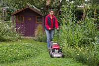 Creating a Clover mound - Woman mowing the lawn in her back garden.