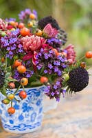 Floral display of rose hips, helianthus seed heads, verbena and chrysanthemum in blue and white tea cup. 