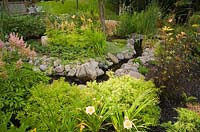 Man made creek through garden borders with peach coloured Hemerocallis - Daylilies and Spiraea bumalda 'Golden Elf' - Spirea shrubs, Pink Astilbe x arendsii on the left and Physocarpus opulifolius 'Coppertina' - Ninebark shrub on the right