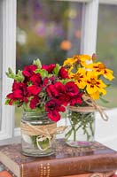Floral display of Pelargonium 'Lord Bute' and Tagetes 'Naughty Marietta' in glass jars with a view through a window to the garden