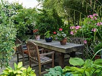 A private patio seating area with chunky wooden table and chairs in a very small space. Large-scale furnishings, as opposed to lots of little bits, increase the sense of roominess in a confined space. Tall bamboo screens the seating from the main garden.