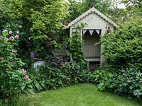 A traditional summer garden with borders filled with roses and perennials with a wooden arbour.
