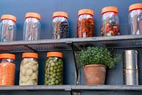 Shelves of jars of olives, pickles and a pot of thyme.