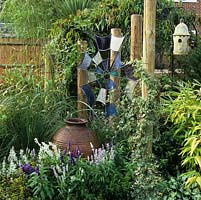 Stained glass spiders web suspended from ivy clad wooden posts. Blue salvia spires around huge pot below handcrafted, 