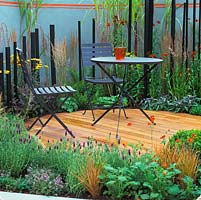 Timber deck has coordinated, black chairs, table and timber verticals in planting of grasses, helenium, achillea, sedum, box balls, lavender, sage and geum.