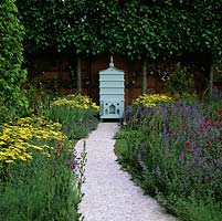 By pleached lime hedge, beehive at end of path made from pebbles set in concrete. Plants: achillea, lavender, catmint, cirsium and valerian.