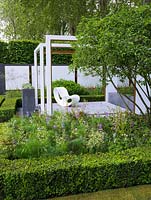 Pergola like wooden frames focus attention on views within the space. Geometric layout of box and hornbeam mixes with perennials and shrubs. Raised patio with chair.