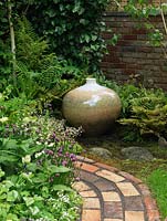 Brick path circles bed of chives, foxglove and saxifrage. In shady corner surrounded by ferns, a lovely pot with crystalline glaze by potter John Stroomer.