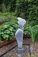 A contemporary stone balancing sculpture by Andrian Gray alongside irises planted in a gentle garden stream.