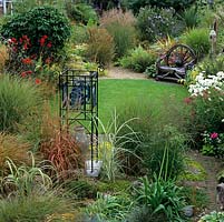 Stained glass obelisk amidst miscanthus, bamboo, carex, molinia and agapanthus seed heads. Autumn perennials - cosmos, sedum, dahlia - in beds with grasses.