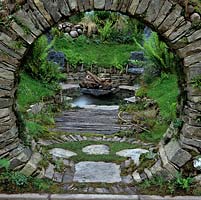 Glimpsed through a circular, dry stone window, a tranquil, personal sanctuary, naturalistic in style, with pool and seats.
