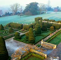 Planted in 1901, formal parterre of box hedges and giant yew topiary shapes - cones, spirals, pyramids, domes and birds. Dawn mist rises from River Thames.