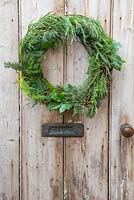 Mixed Evergreen Wreath hanging on a wooden door. Foliage contains Sequoiadendron giganteum, Pinus, Larch and Ilex aquifolium