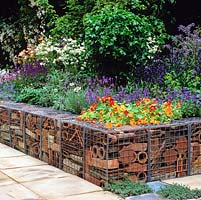 Low retaining wall made from galvanised cages filled with reclaimed terracotta pipes, tiles and pots. Raised bed of nasturtium, lavender, salvia, borage, aquilegia.